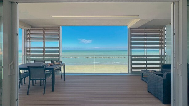 Een balkon met uitzicht op het strand, een tafel met stoelen en een bank.