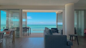 Een moderne woonkamer met een grote glazen deur die leidt naar een balkon met uitzicht op een strand.