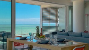 Een eetruimte met uitzicht op de oceaan, een gedekte tafel met borden, kommen en glazen, en een bank op de achtergrond.