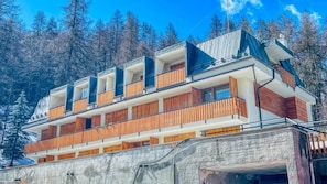 A multi-story hotel with balconies, a stone facade, and a forested backdrop.