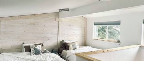 Une chambre avec deux lits, une tête de lit en bois, une fenêtre avec des stores et un luminaire au plafond.