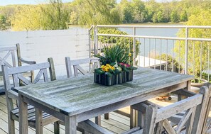 Eine Holzterrasse mit Tisch und Stühlen, mit Blick auf ein Gewässer, umgeben von Bäumen.