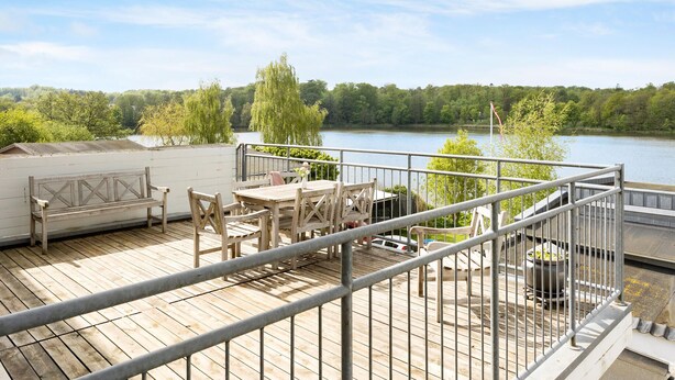 A wooden deck with outdoor furniture overlooking a lake, surrounded by trees. - 1 bedroom gorgeous home in Gråsten (Gråsten)