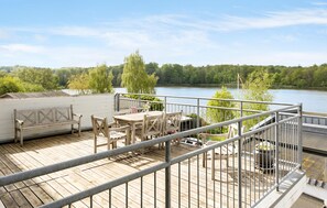 Eine Holzterrasse mit Gartenmöbeln Blick auf einen See, umgeben von Bäumen.
