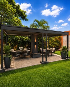 A covered outdoor patio with a table and chairs, surrounded by greenery and a clear sky. - La Belva Court (Lusaka)