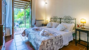 A bedroom with a bed, a nightstand, a lamp, and a view of the garden. - Le Monache - intero nucleo by Interhome (Montaione)