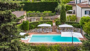A pool area with lounge chairs and umbrellas, surrounded by lush greenery and stone walls. - Monache 4 by Interhome (Montaione)