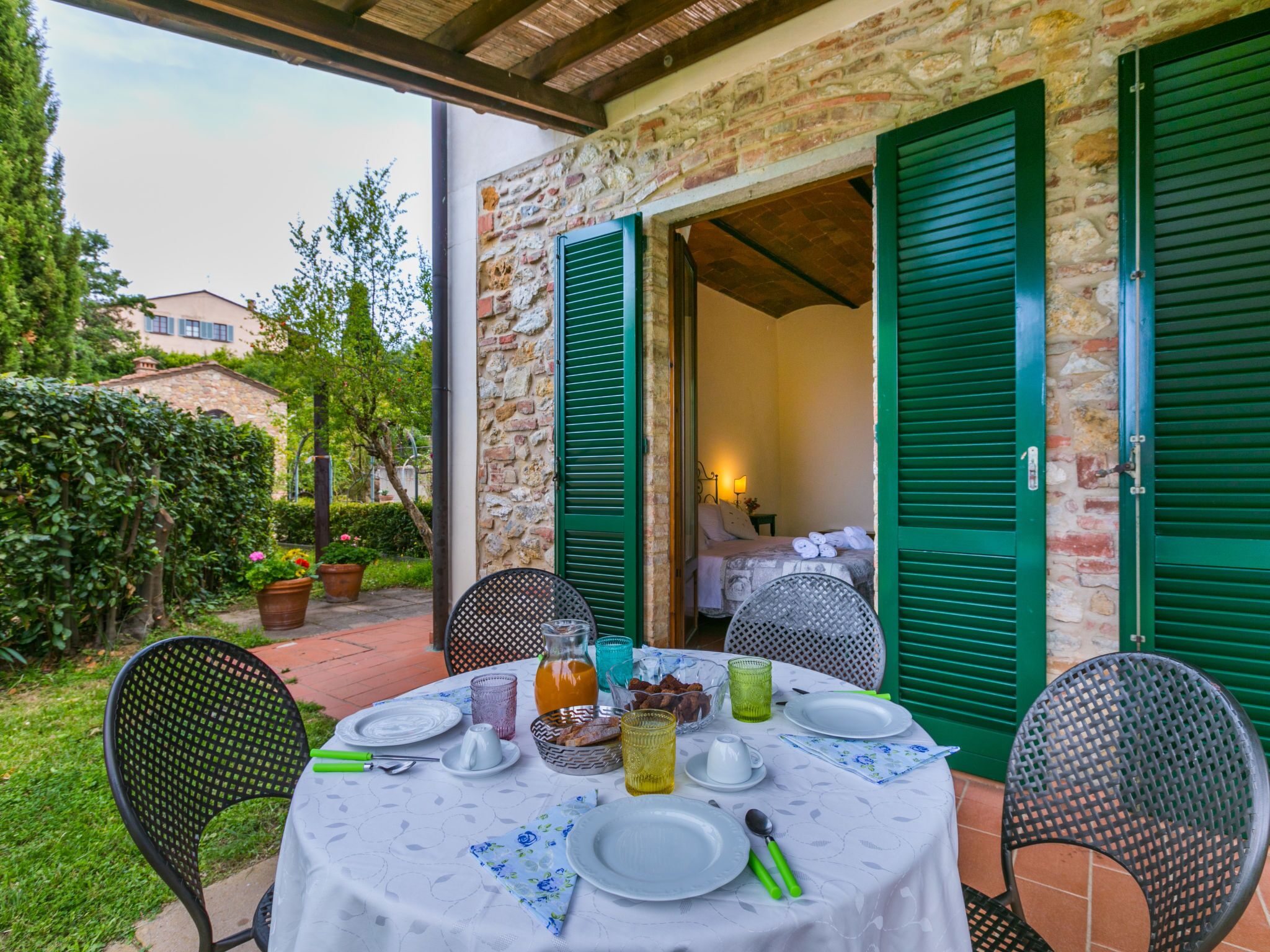 A table set for breakfast with a view of a bedroom through open shutters.
