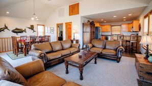 A spacious living room with leather sofas, a wooden coffee table, and a dining area with wooden chairs and a table. - Pet Friendly, fenced in Yard and Huge Pool! Sound Views, 2 min walk to Ocean (Waves)