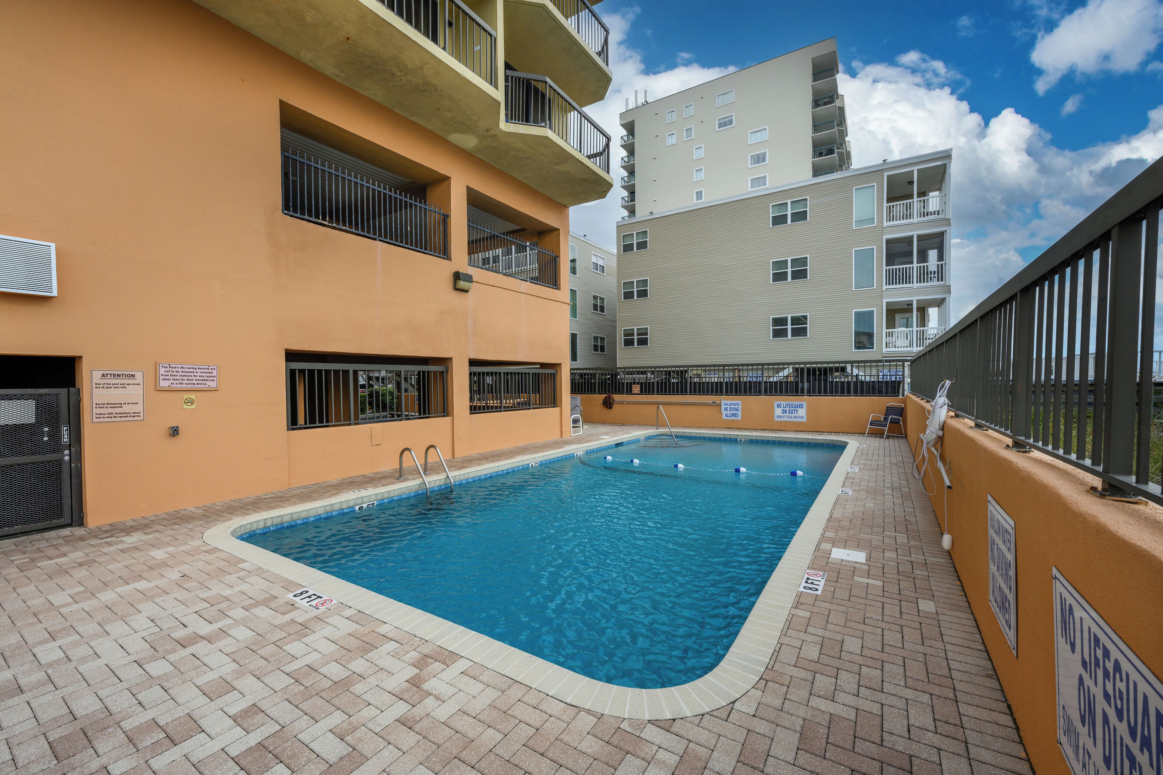 Une piscine dotée d’une terrasse carrelée, entourée d’immeubles à plusieurs étages, avec des balcons et des fenêtres.