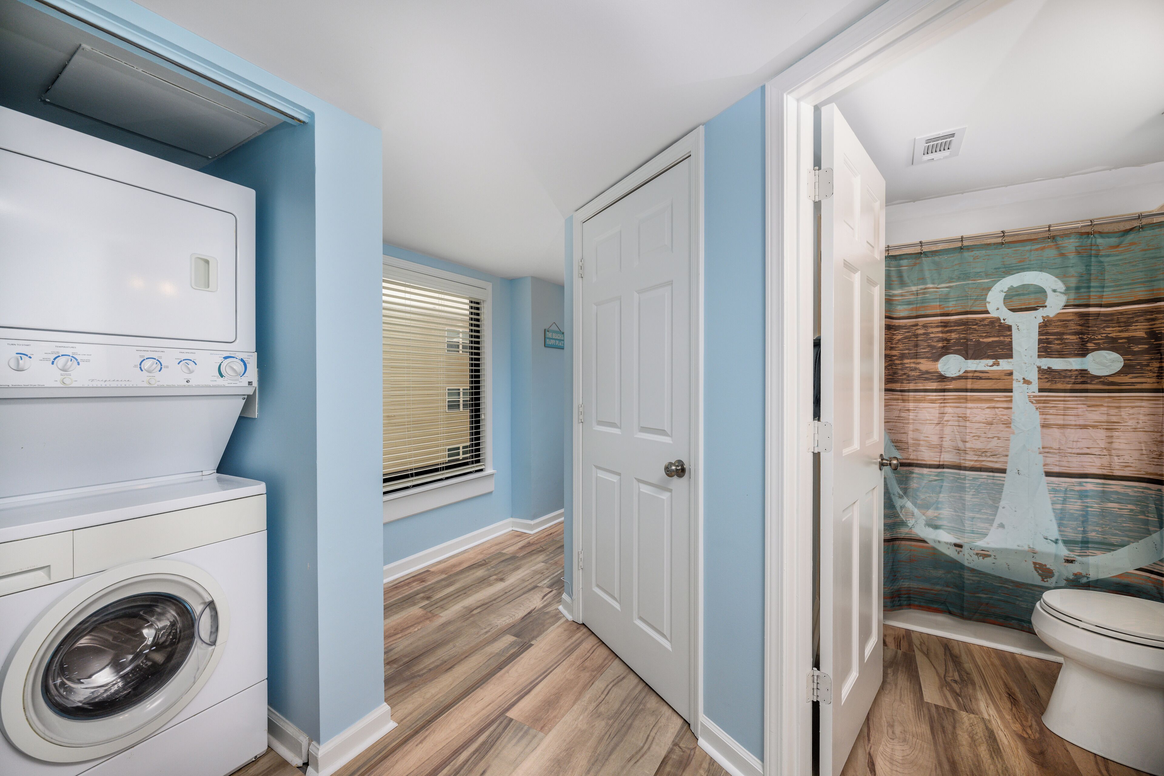 A laundry room with a washing machine and dryer, a door leading to a bathroom with a striped shower curtain, and a window with blinds.