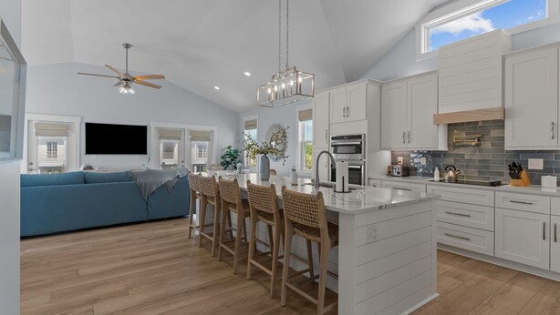A modern kitchen with white cabinetry, a central island with bar stools, and a ceiling fan.