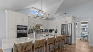 A modern kitchen with white cabinetry, stainless steel appliances, a marble island with bar stools, and a pendant light.