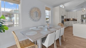A modern kitchen with white cabinets, a dining area with a wooden table and white chairs, and a large mirror on the wall.