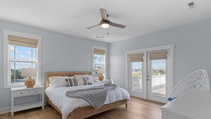 A bedroom with a bed, bedside tables, a ceiling fan, and a view through the glass doors.