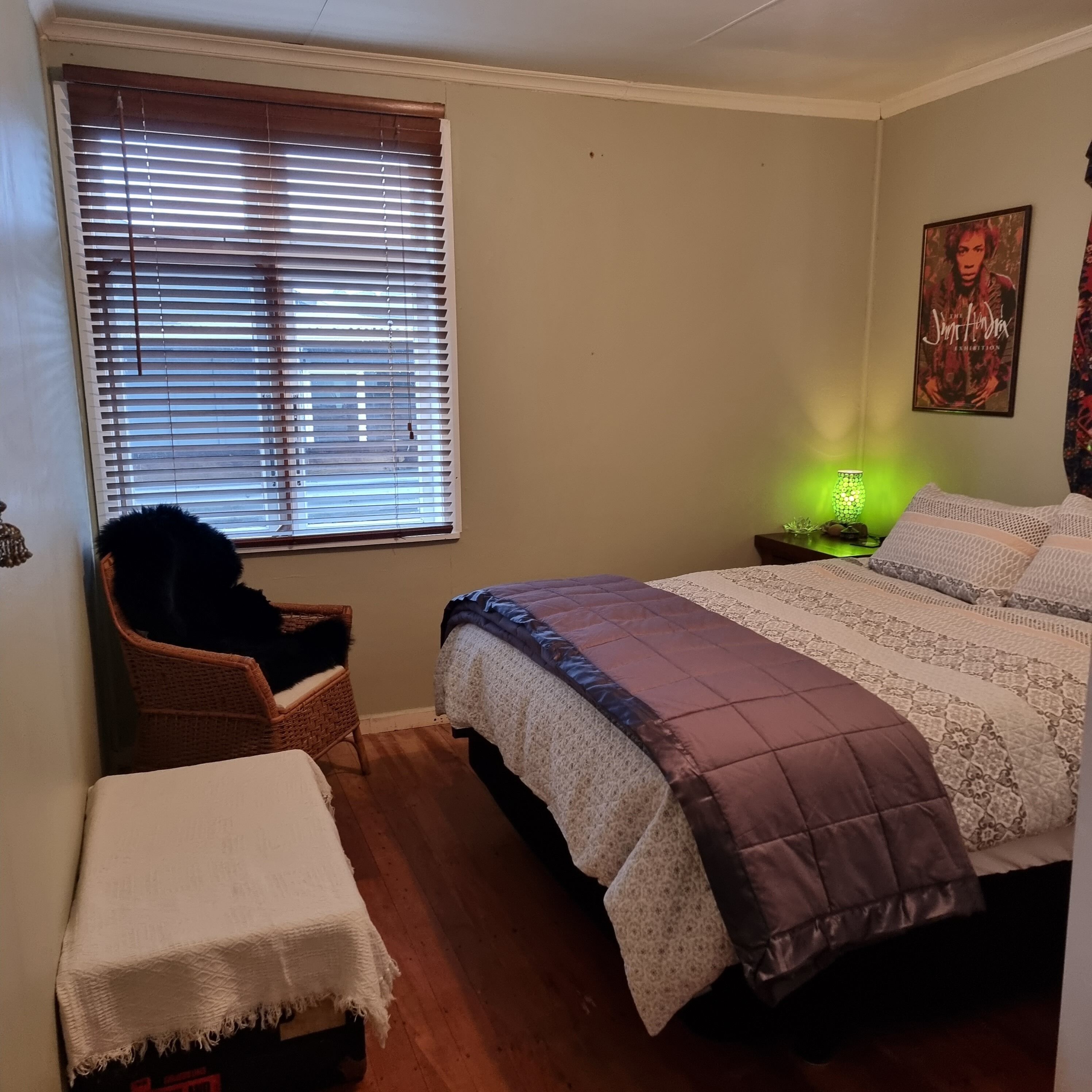 A bedroom with a bed, a chair, a nightstand with a lamp, and a poster on the wall.
