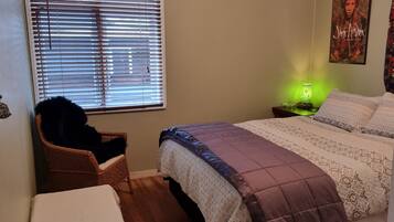 A bedroom with a bed, a chair, a nightstand with a lamp, and a poster on the wall.