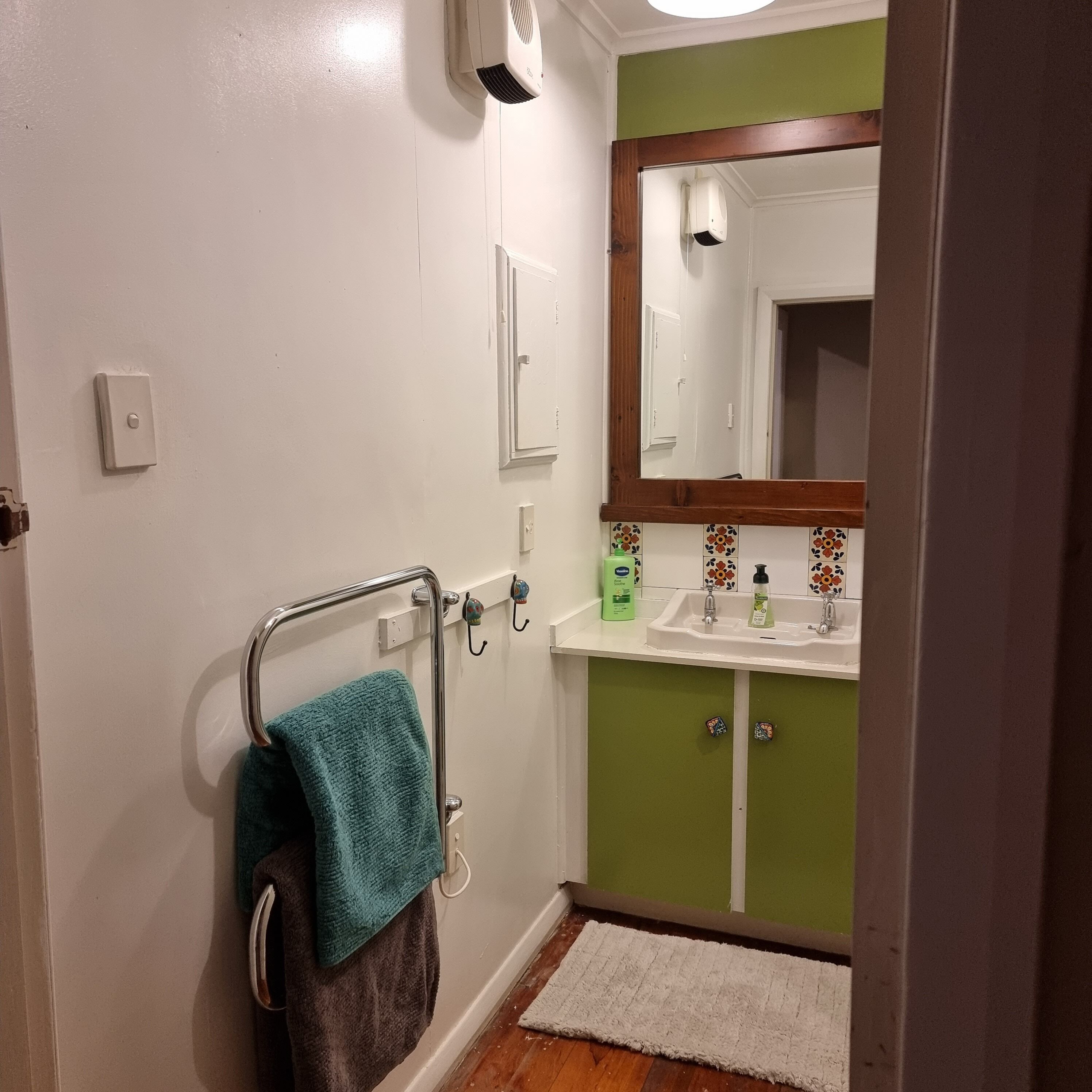 A bathroom with a white sink, green cabinet, and a mirror above it. There is a towel rack with a blue towel and a brown towel hanging on it.