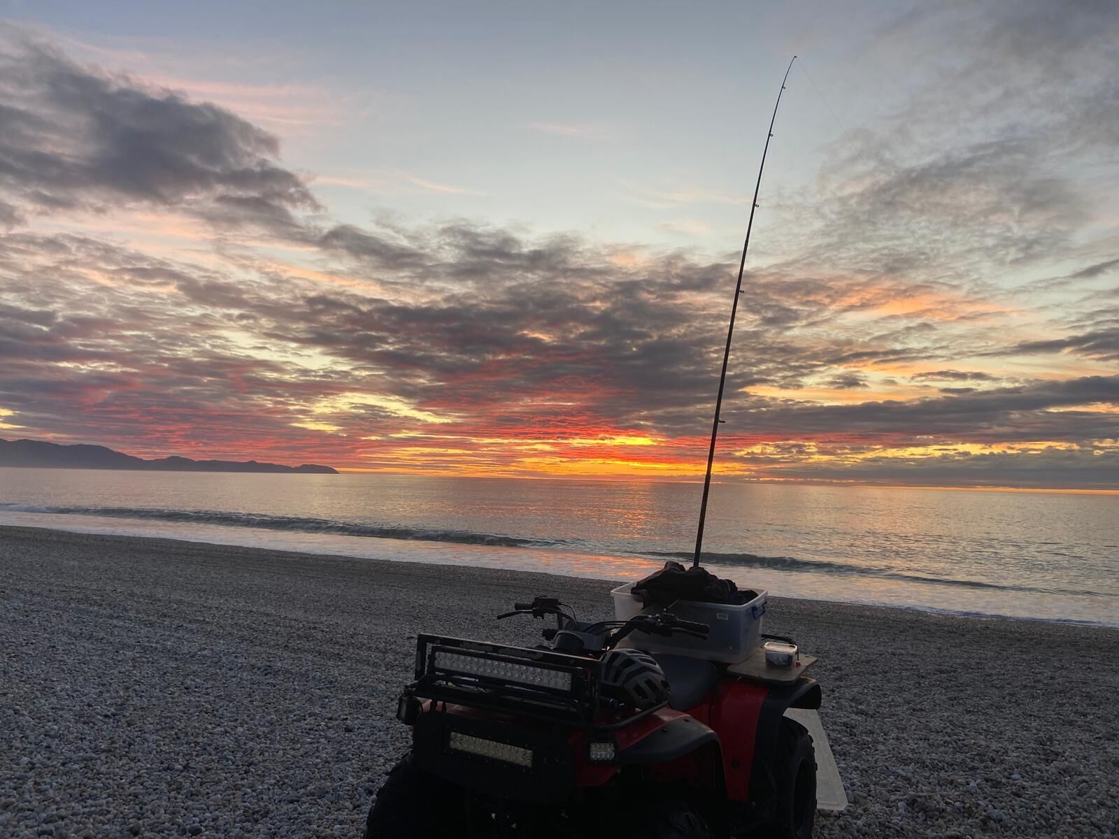 A quad bike on a pebbled beach with a sunset in the background.