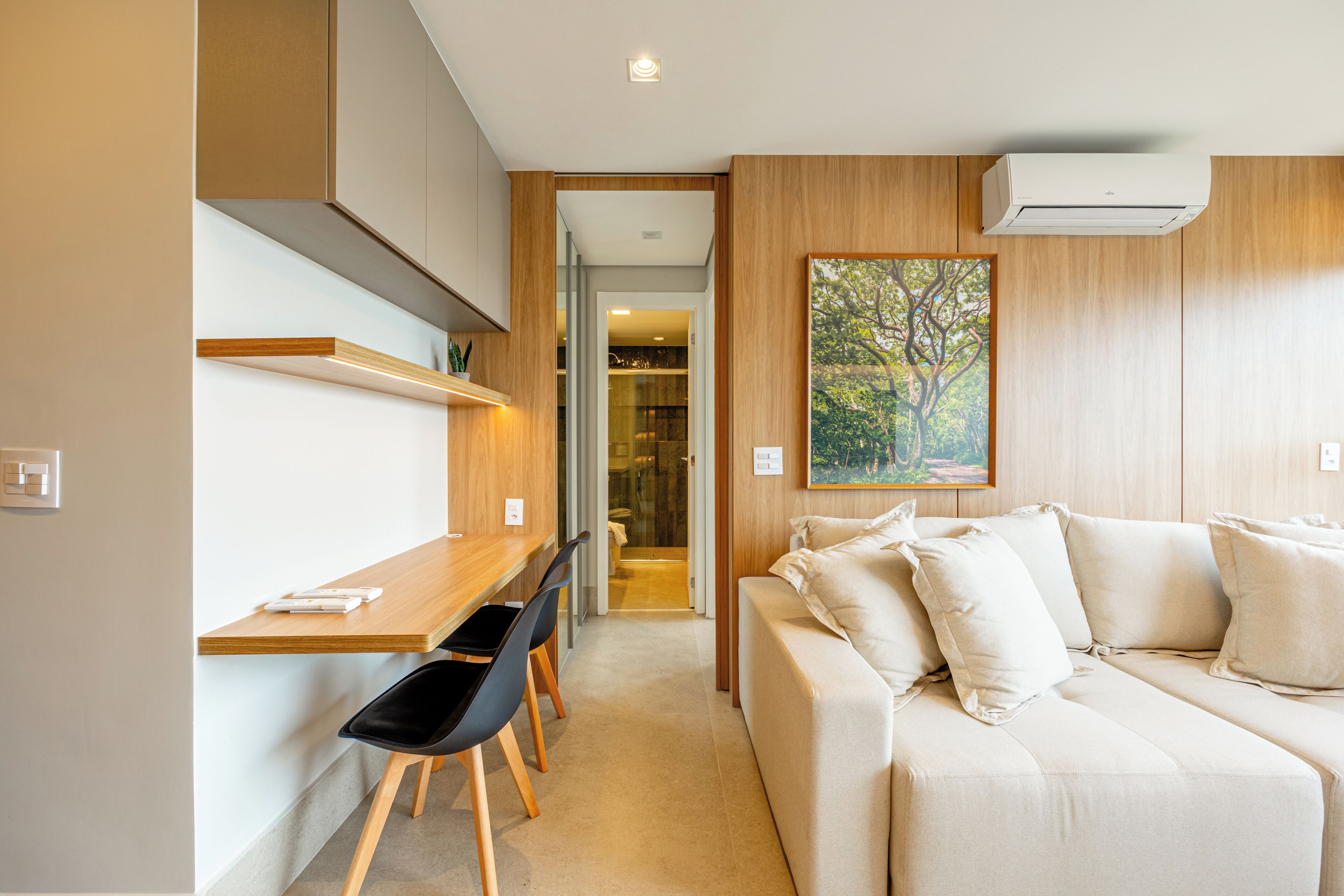 A modern room with a wooden desk, black chairs, a beige sofa, and a painting of a tree.