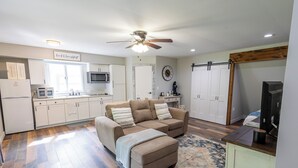 A compact living space with a kitchenette, a sofa, a coffee table, and a ceiling fan. - Tranquil creek side retreat (Canandaigua)