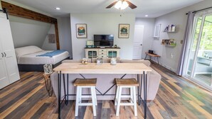 A cozy room with a bed, a kitchen area with a bar, and a large window. - Tranquil creek side retreat (Canandaigua)