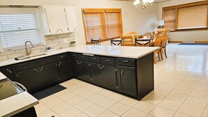 A modern kitchen with black cabinets, a white countertop, and a dining area with wooden chairs and a table. - 3B Spacious Home+ Free Parking near Chicago O'Hare (Franklin Park)