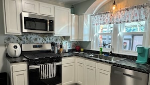Una cucina con mobili bianchi, un piano cottura in acciaio inossidabile, un forno a microonde ed una lavastoviglie.
