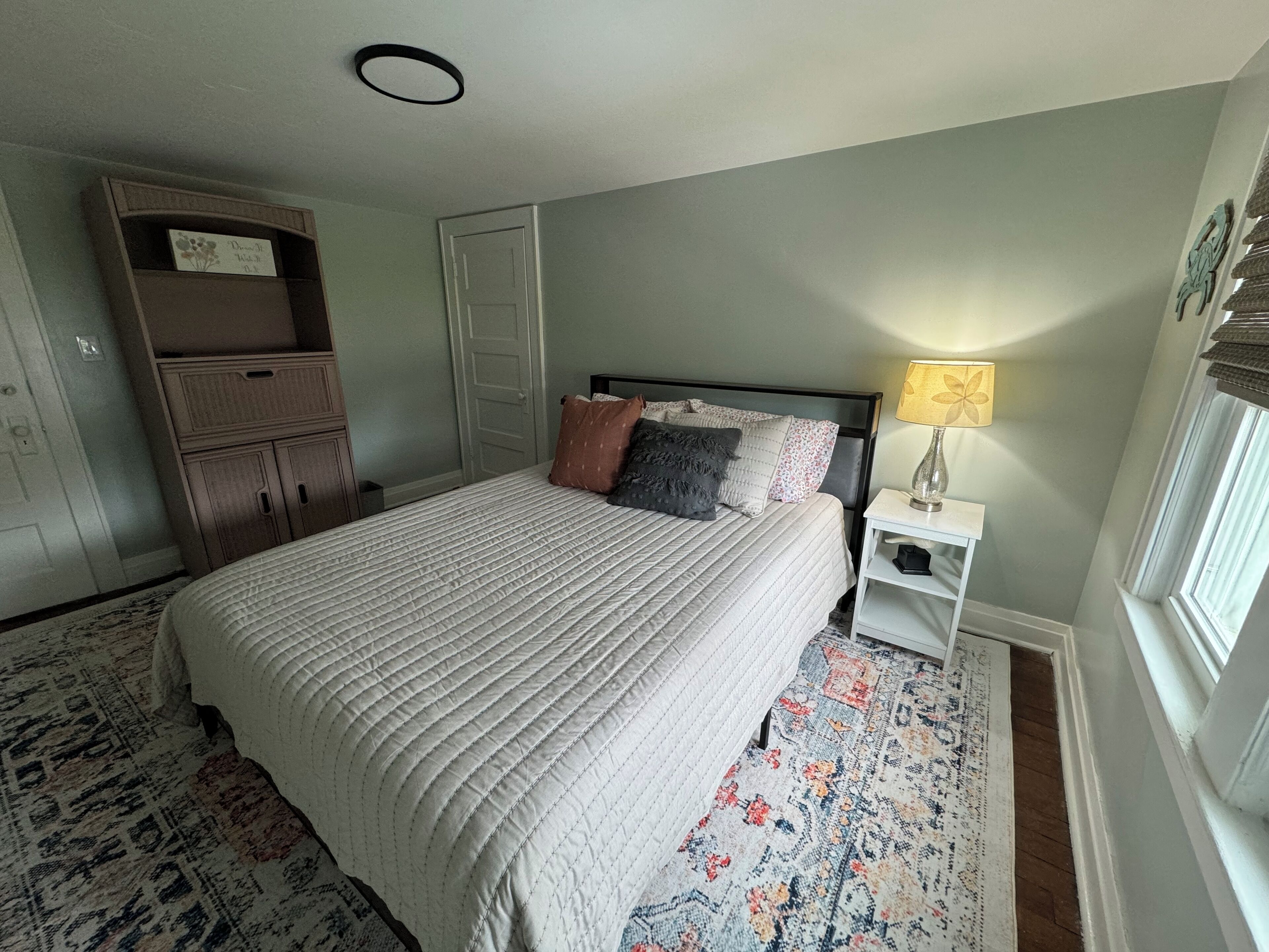 A bedroom with a bed, nightstand, dresser, and a window with blinds.