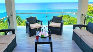 A covered outdoor seating area with wicker furniture and a table, overlooking a scenic ocean view.
