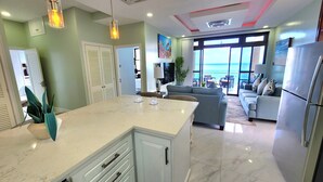 A modern kitchen with a large island, a dining area with a view, and a living room with a sofa and a TV.