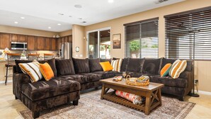 A spacious living area with a dark brown sectional sofa, a wooden coffee table, and a kitchen in the background. - Desert Oasis w/Pool, Spa & more! (Coachella)
