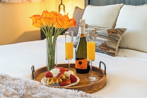 A breakfast tray with waffles, strawberries, whipped cream, and a bottle of Prosecco on a bed.
