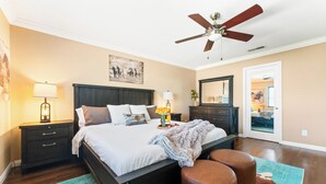A bedroom with a bed, bedside lamps, a ceiling fan, a nightstand, a dresser, and a mirror. - Desert Oasis w/Pool, Spa & more! (Coachella)