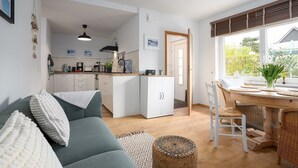 A modern kitchen with white cabinets, a dining area with a round table, and a cozy living space with a sofa and a patterned rug.