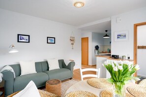 Una sala de estar moderna con un sofá verde, una mesa de comedor con individuales tejidos y un jarrón con tulipanes blancos.