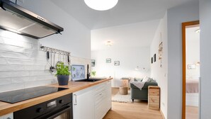 A modern kitchen with white cabinets, a black stove, and a wooden countertop. There is a potted plant on the counter and a small table with a plant beside the kitchen.
