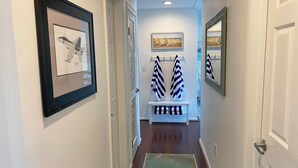 A hallway with framed artwork, a bench with striped towels, and a mirror on the wall. - Vacationing is easy in this newly refreshed beach condo! (Virginia Beach)