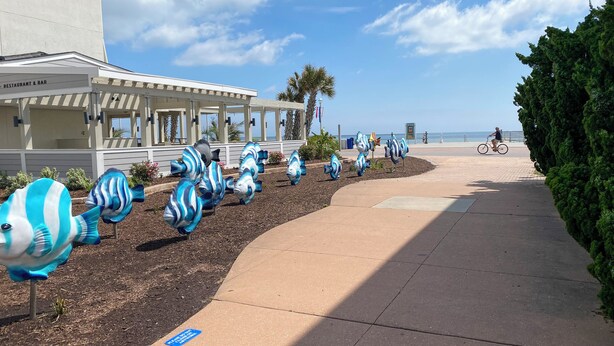 A coastal walkway with decorative fish sculptures, a covered outdoor seating area, and a clear view of the ocean. - Vacationing is easy in this newly refreshed beach condo! (Virginia Beach)