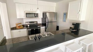 A modern kitchen with white cabinets, stainless steel appliances, a granite countertop, and a black backsplash. - Vacationing is easy in this newly refreshed beach condo! (Virginia Beach)