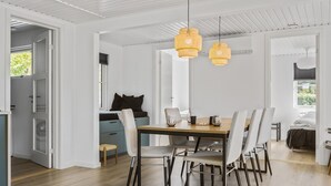 Comedor con mesa y sillas de madera, dos lámparas colgantes de ratán y vista al exterior a través de una puerta.