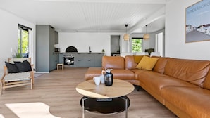 Una sala de estar moderna con un sofá de cuero, una mesa de centro de madera y una cocina al fondo.