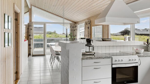 A modern kitchen with a central island, white cabinetry, and a large window offering a view of the outdoors. - Stunning home in Henne with sauna (Henne)