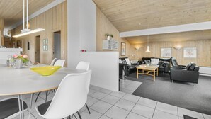 A spacious living area with a high ceiling, wooden beams, a dining table with chairs, a black leather sofa, and a coffee table. - Stunning home in Henne with sauna (Henne)