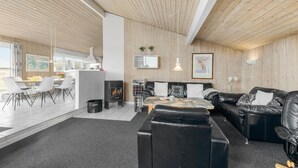 A modern living room with a fireplace, leather sofas, and a dining area with white chairs. - Stunning home in Henne with sauna (Henne)