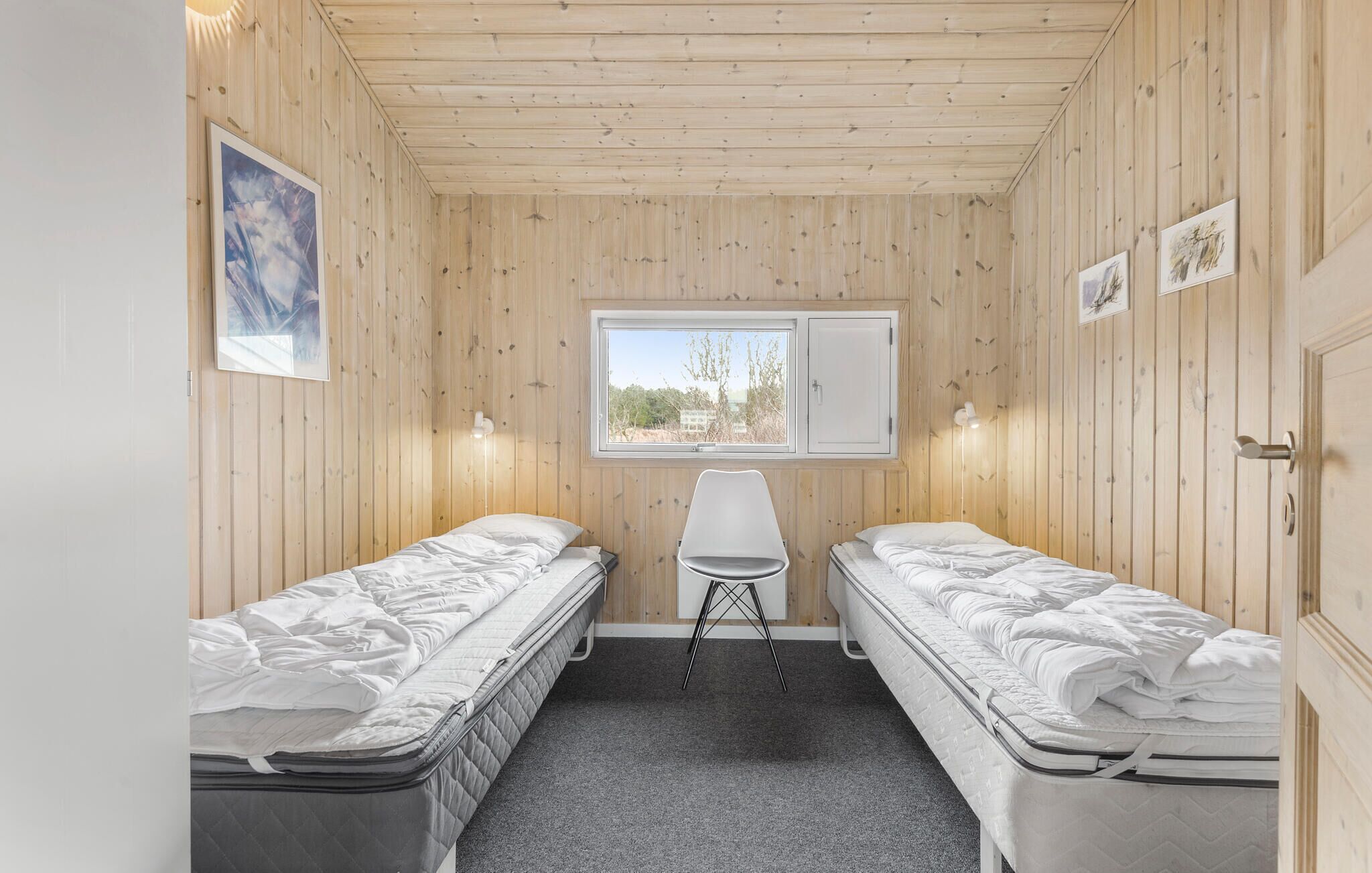 Una habitación pequeña con paneles de madera, dos camas individuales, una ventana y un escritorio.