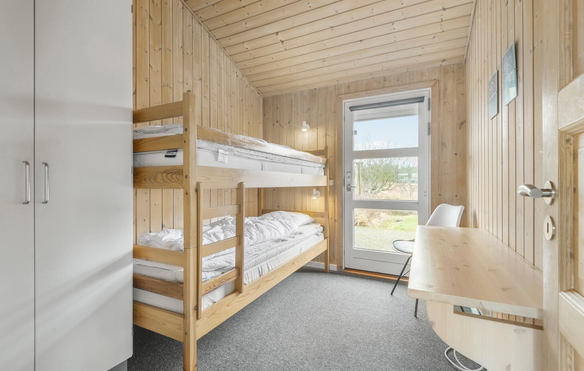 A bunk bed room with a desk and a door leading outside.