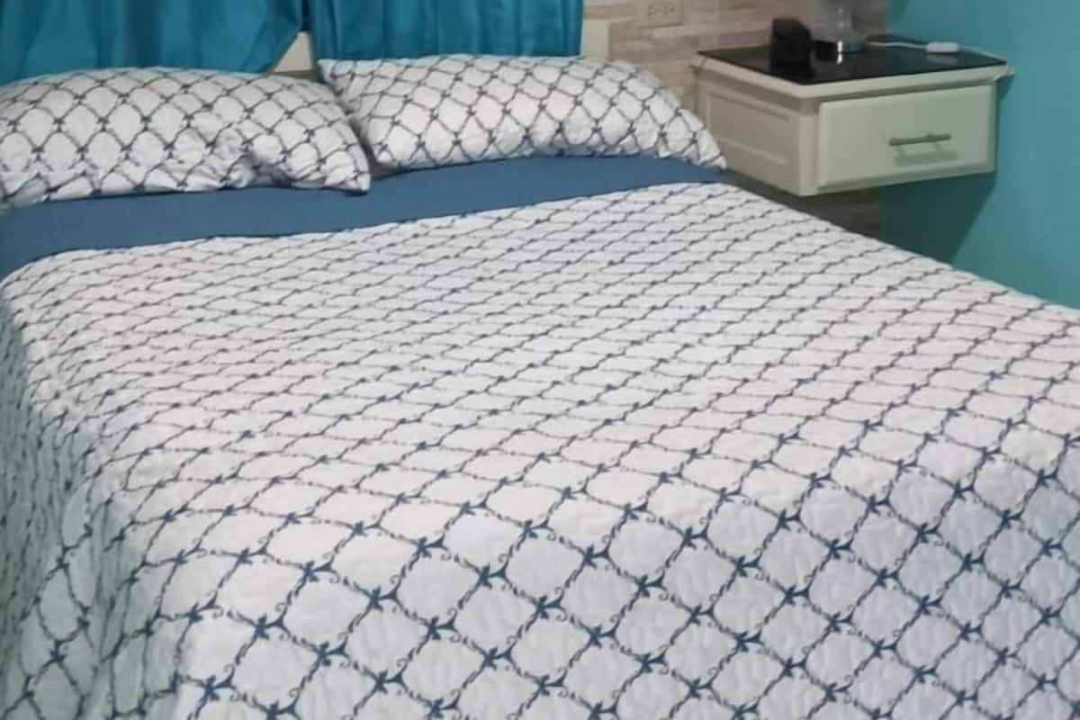 Un dormitorio con cama, cortinas, una mesita de noche y un aire acondicionado.