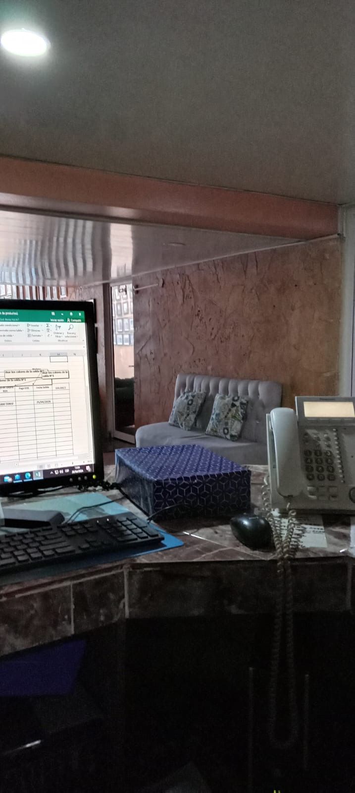A room with a computer desk, a telephone, a cushioned seating area, and a window.