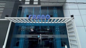 Une entrée d’hôtel moderne avec une façade en verre et une enseigne indiquant « HÔTEL FRANO ».